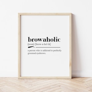 以下が含まれることがあります： 「browaholic」という単語が黒い太字で書かれた額入りのプリント。その下に定義があり、「完璧に手入れされた眉毛に夢中になっている人」と書かれています。フレームは明るい木の色で、背景は白です。