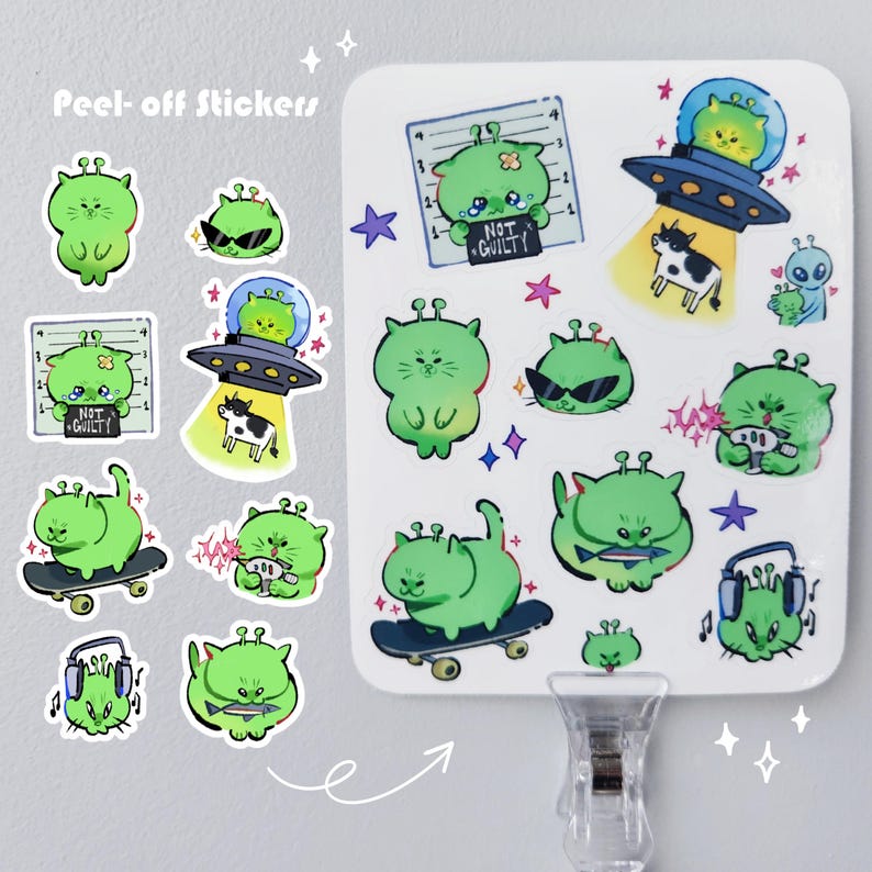 May include: A collection of green alien cat peel-off stickers. The stickers feature various designs, including aliens in a spaceship, wearing sunglasses, and holding a sign that says "NOT GUILTY". Some stickers are on a skateboard or wearing headphones.