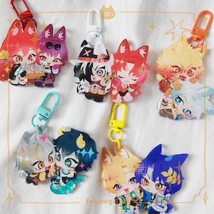 May include: A selection of anime-style character keyrings in various colours. Each keyring showcases a unique design with vibrant hues, including red, blue, yellow, and purple. The keyrings are attached to different coloured clasps, set against a white fabric background.
