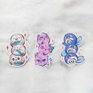 Puede incluir: Tres dise&ntilde;os de pegatinas con personajes de dibujos animados apilados. Un dise&ntilde;o muestra tres b&uacute;hos con pajaritas, otro muestra tres criaturas rosas con forma de gato y el &uacute;ltimo muestra tres criaturas azules con forma de foca. Cada dise&ntilde;o tiene un acento de estrella brillante.