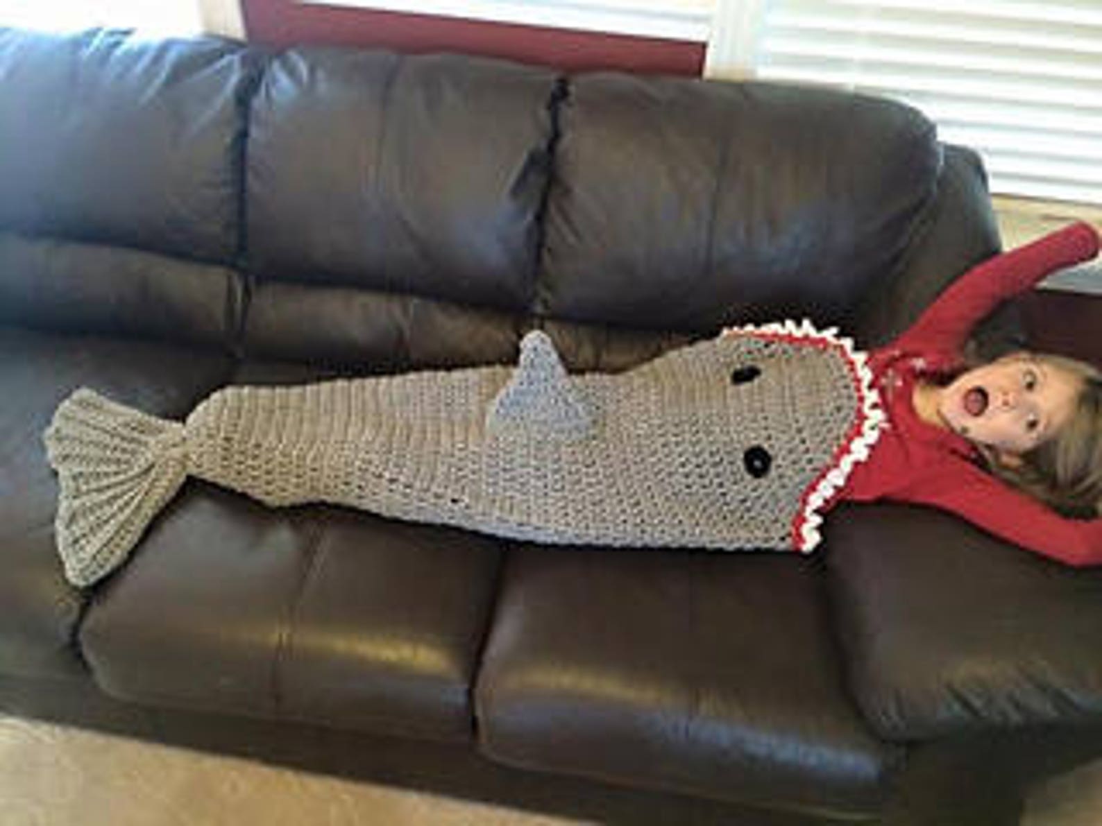 Crochet Shark Tail Blanket Pattern Crochet shark tail blanket in soft gray yarn, shaped like a shark fin and perfect for kids to snuggle in during movie nights.