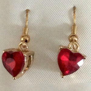 May include: A pair of gold heart-shaped earrings with red crystal stones.