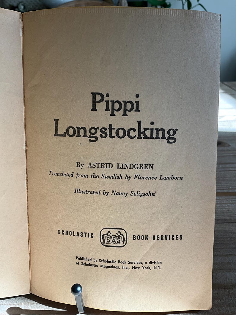 Może przedstawiać: Otwarta strona książki z tytułem "Pippi Longstocking" pogrubioną czcionką. Wymieniono r&oacute;wnież autora, tłumacza i ilustratora. Widoczne jest logo Scholastic Book Services. Strona ma wygląd vintage, postarzaną.