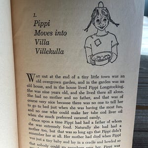 Może przedstawiać: Otwarta strona książki z tekstem i czarno-białą ilustracją dziewczynki z warkoczami. Tekst brzmi "Pippi wprowadza się do Villa Villekulla".