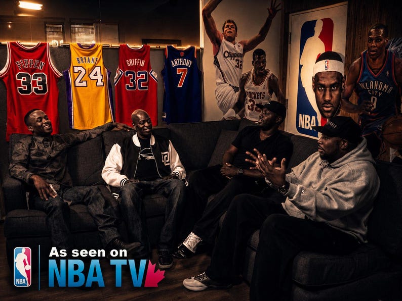 May include: A group of men seated on a dark gray sofa, with basketball jerseys hanging on the wall behind them. The jerseys are red, yellow, and blue, with player names and numbers. The NBA logo and "As seen on NBA TV" are visible.