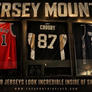 May include: Three framed sports jerseys displayed in shadow boxes. The jerseys are red with "RODMAN 91", black with "CROSBY 87", and blue with "IVERSON 3". The text "JERSEY MOUNTS" is at the top. The text "MAKE YOUR JERSEYS LOOK INCREDIBLE INSIDE OF SHADOW BOXES" is at the bottom.