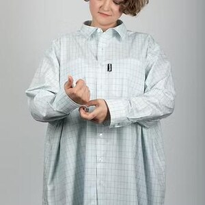 May include: A light blue and white plaid button-down shirt. The shirt has long sleeves and a chest pocket with a small black tag. The shirt is oversized and appears to be made of a lightweight fabric.