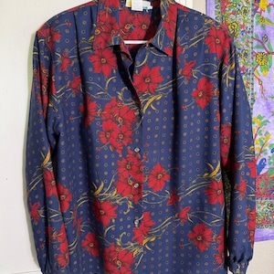 May include: A long-sleeved button-down shirt in navy blue featuring a repeating pattern of red flowers with yellow stems and small gold-colored dots. The shirt has a pointed collar, a front button placket, and buttoned cuffs on the sleeves.