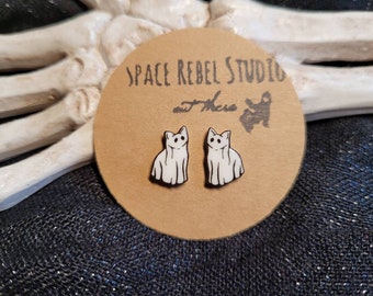 May include: A pair of white ghost cat stud earrings on a brown card with the text "Space Rebel Studio" and a small ghost cat illustration.