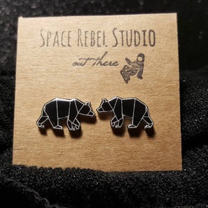 May include: A pair of black geometric bear stud earrings on a brown card with the text "Space Rebel Studio out There".