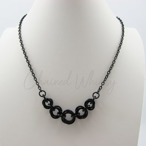 May include: A black chain necklace with a five-ring pendant. The rings are interlocked and form a geometric pattern.
