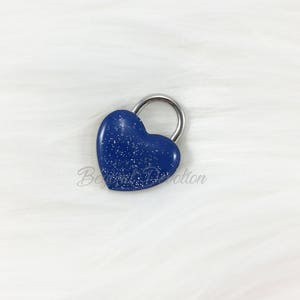 May include: A small blue heart-shaped padlock with a silver metal loop. The padlock has a sparkly finish.