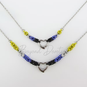 May include: Two silver chain necklaces with heart-shaped pendants. The chains are made of silver, black, and blue wire, with yellow accents. The necklaces are layered, with the shorter necklace on top.