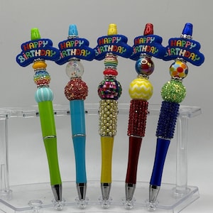 May include: Five colorful pens with "Happy Birthday" on the top. Each pen has a different color and design of beads.