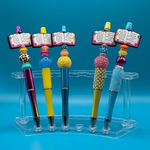 May include: Five colorful pens with book-shaped tops. Each pen has a different color and design. The tops of the pens have the text "In a really good place right now" and "In my book of course not mentally".