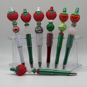 以下が含まれることがあります： イチゴの形をしたトップが付いた緑と赤のペンが7本。ペンはビーズとラインストーンで飾られています。