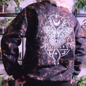 May include: Black sweatshirt with a white bleached design of a moth with geometric shapes and crescent moons.