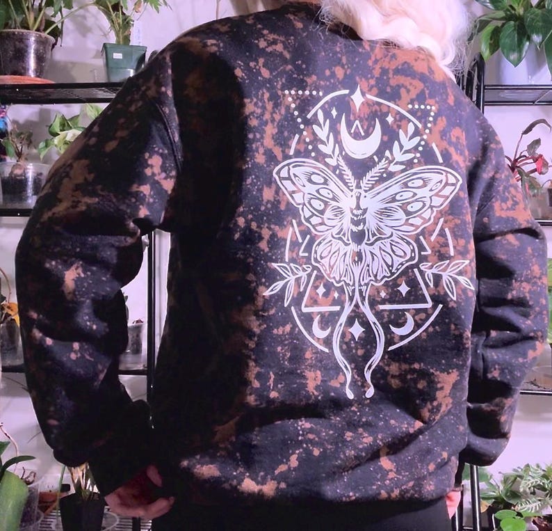 May include: Black sweatshirt with a white bleached design of a moth with geometric shapes and crescent moons.