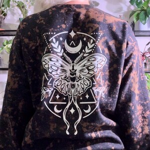 May include: Black sweatshirt with a bleached effect and a white graphic print of a moth with crescent moons and stars.