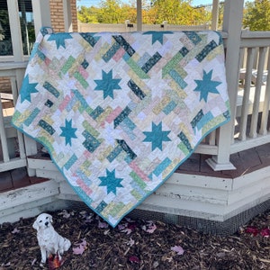 May include: A teal and white patchwork quilt with a star pattern. The quilt is made with a variety of floral fabrics and is displayed on a wooden porch.