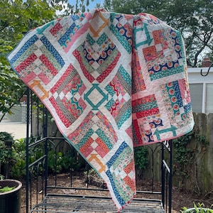 May include: A patchwork quilt with a white background and squares of various colors, including red, pink, blue, green, and yellow. The quilt is made of different fabrics with floral and geometric patterns.