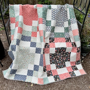 May include: A patchwork quilt with a variety of floral and geometric patterns in shades of pink, green, blue, and black. The quilt is made of cotton fabric and has a white backing.