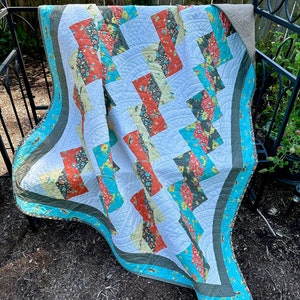 May include: A quilt with a patchwork design featuring a variety of floral patterns in shades of red, orange, yellow, green, and blue. The quilt is bordered with a turquoise and green trim.