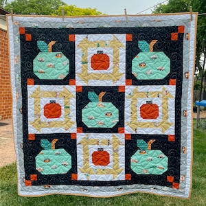 May include: A quilt with a black background and a patchwork design featuring green apples with white camper vans, orange pumpkins, and white and yellow squares.