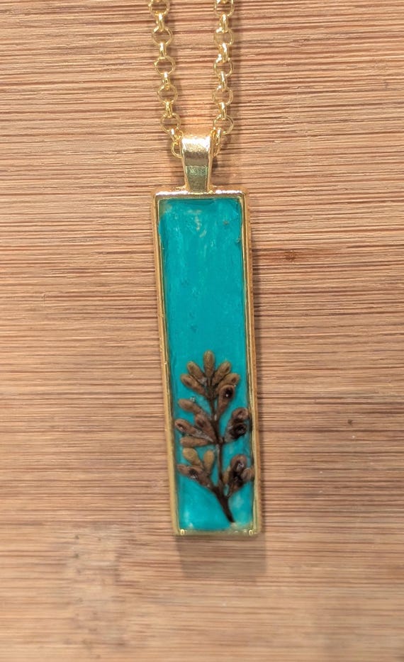 SERENITY CALLING: Statement pendant with authentic botanicals, pigment, and resin. Gold tone.