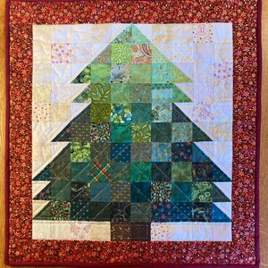 May include: A quilted Christmas tree wall hanging. The tree is made of various green patterned squares. The background is white with a red border featuring a floral pattern. The tree is centered on the quilt.