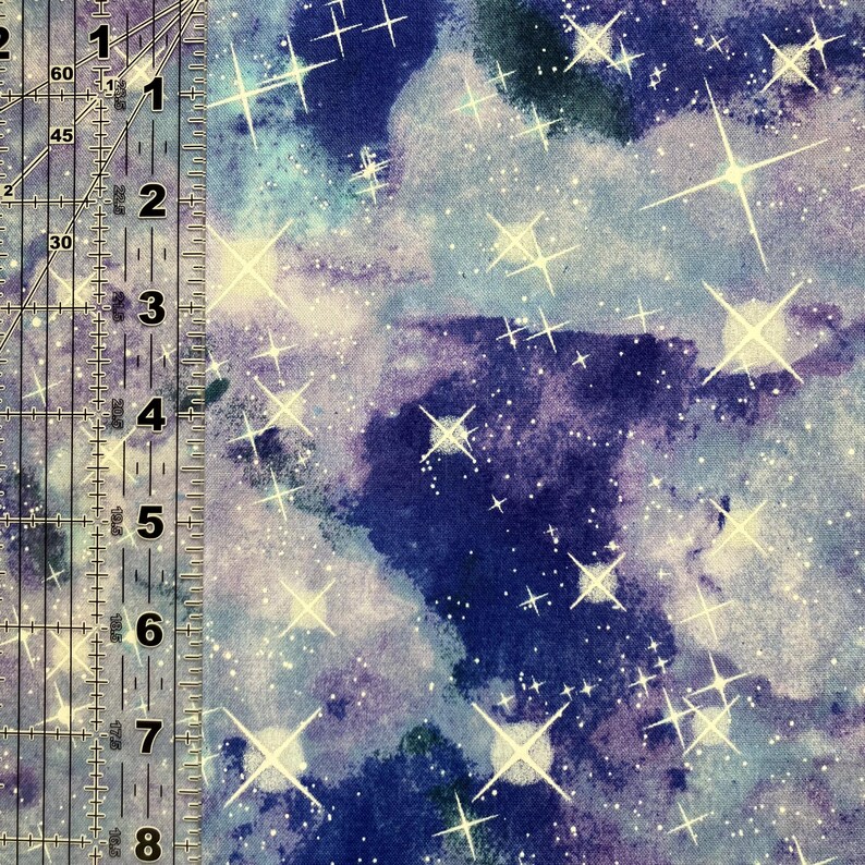 Puede incluir: Tela con un dise&ntilde;o celestial que presenta un fondo de acuarela azul oscuro y p&uacute;rpura. Estallidos de estrellas blancas y brillantes y diminutos puntos blancos est&aacute;n dispersos por la tela. Una regla est&aacute; en el lado izquierdo.