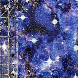 Puede incluir: Primer plano de una tela con un dise&ntilde;o de galaxia vibrante. La tela presenta un fondo azul profundo con patrones arremolinados, estrellas blancas y una dispersi&oacute;n de peque&ntilde;os puntos blancos. El dise&ntilde;o evoca el cosmos.