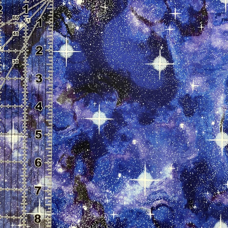 Puede incluir: Primer plano de una tela con un dise&ntilde;o de galaxia vibrante. La tela presenta un fondo azul profundo con patrones arremolinados, estrellas blancas y una dispersi&oacute;n de peque&ntilde;os puntos blancos. El dise&ntilde;o evoca el cosmos.