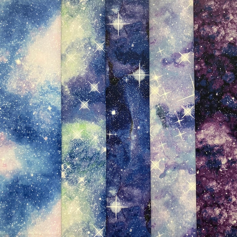 Puede incluir: Muestras de tela con un dise&ntilde;o de galaxia. La tela tiene un efecto de acuarela con tonos de azul, morado y blanco, y est&aacute; salpicada de formas blancas en forma de estrella. Las muestras est&aacute;n dispuestas verticalmente.