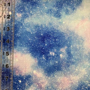 Puede incluir: Tela con un dise&ntilde;o celestial que presenta un patr&oacute;n de galaxia azul y p&uacute;rpura con motas blancas. Una regla est&aacute; en el lado izquierdo de la imagen, mostrando medidas en cent&iacute;metros.