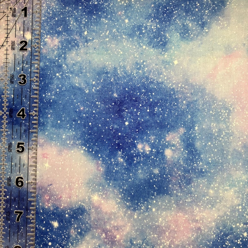 Puede incluir: Tela con un dise&ntilde;o celestial que presenta un patr&oacute;n de galaxia azul y p&uacute;rpura con motas blancas. Una regla est&aacute; en el lado izquierdo de la imagen, mostrando medidas en cent&iacute;metros.