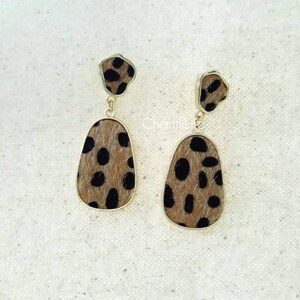 May include: A pair of dangle earrings with a gold-colored frame. The earrings feature a brown and black spotted pattern. The top portion of the earrings is a small, irregular shape, while the bottom portion is an elongated teardrop shape.