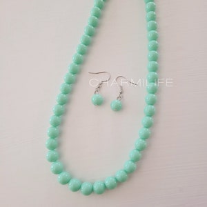 May include: A mint green beaded necklace and matching earrings. The necklace is made of round beads and has a silver clasp. The earrings are also made of round beads and have silver hooks.