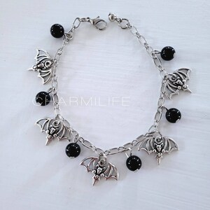 May include: A silver chain bracelet with black beads and bat charms. The bracelet has a lobster clasp closure.