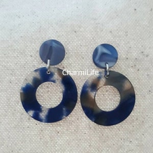 May include: A pair of blue and white marbled acrylic earrings. Each earring features a small circular stud connected to a larger, open circle. The earrings have a marbled pattern with the text "CharmiLife".