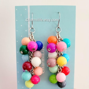May include: A pair of dangle earrings featuring clusters of colorful beads in various shades. The earrings have silver-tone hooks and chains. The text "Charmilife.etsy.com" is visible on the background.