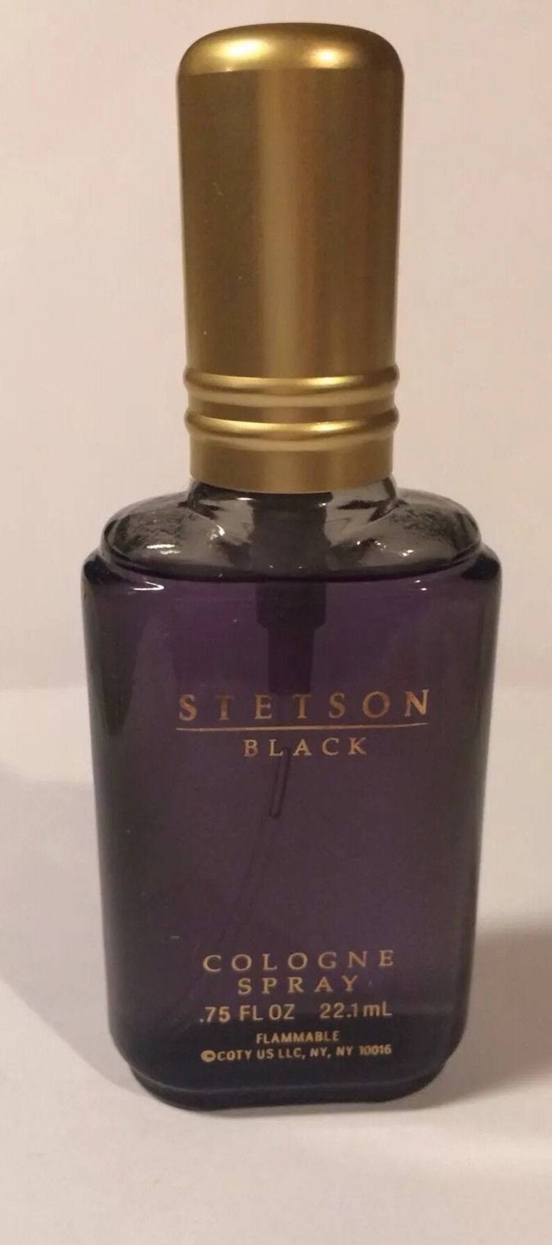 May include: A glass bottle of Stetson Black cologne spray. The bottle is purple with a gold cap and label. The label reads "Stetson Black Cologne Spray .75 fl oz 22.1 ml Flammable Coty US LLC, NY, NY 10016".
