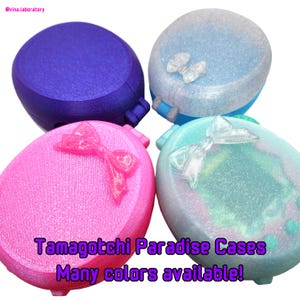 Könnte beinhalten: Vier farbenfrohe Tamagotchi Paradise Cases in Blau, Rosa, Hellblau und Türkis. Jede Hülle hat eine strukturierte Oberfläche und eine dekorative Schleife oder einen Schmetterling. Der Text lautet "Tamagotchi Paradise Cases Many colors available!"
