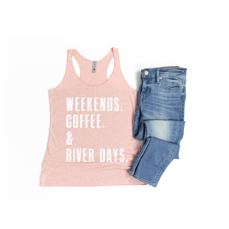 Puede incluir: Un top de tirantes rosa con el texto "Weekends. Coffee. & River Days." impreso en blanco. El top de tirantes se combina con unos vaqueros azules.