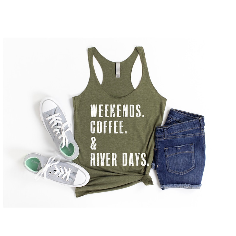 Puede incluir: Una camiseta sin mangas verde con el texto "Weekends. Coffee. & River Days." impreso en blanco. La camiseta sin mangas est&aacute; fotografiada sobre un fondo blanco con un par de zapatillas blancas y unos pantalones cortos de mezclilla azul.
