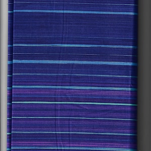 Peut inclure: Un textile plié avec un motif à rayures. Le tissu présente des rayures horizontales dans des tons de bleu, de turquoise et de violet sur un fond bleu foncé. Les rayures varient en largeur et en intensité de couleur, créant un aspect texturé.