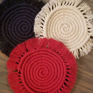 May include: Three round crocheted coasters with fringe. The coasters are in red, white, and black.