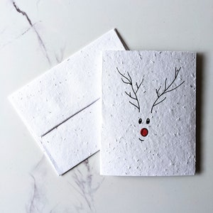 Sobre de tarjeta plantable con semillas de flores silvestres, reno de nariz roja de Navidad sobre papel con semillas de flores silvestres blancas, papel plantable, tarjeta navideña