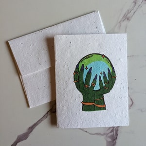 Main de sorcière tenant une boule de cristal sur du papier graine ou une carte en papier blanc aquarelle