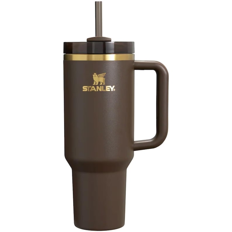 Puede incluir: Un vaso Stanley de color marr&oacute;n oscuro con asa a juego, un logotipo dorado con un oso alado, un borde dorado, una tapa transl&uacute;cida oscura y una pajita central. El recipiente cil&iacute;ndrico tiene una base c&oacute;nica y un asa lateral resistente.